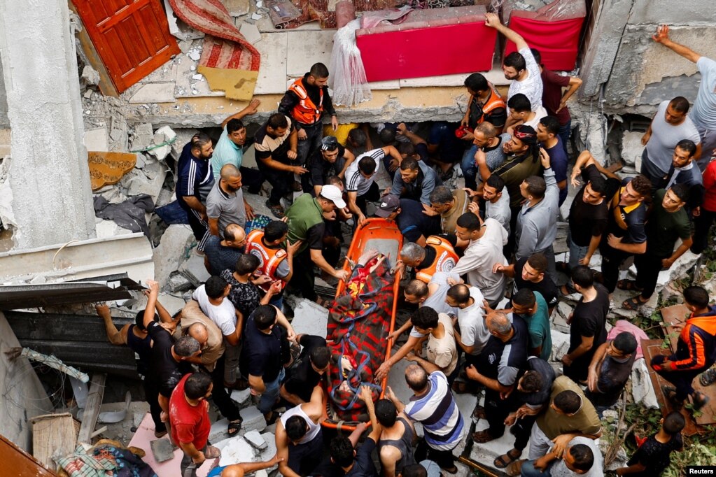 Equipos de rescate y ciudadanos palestinos sacan en camilla a una persona que quedó bajo escombros de una edificación impactada por los ataques. 