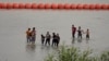 ARCHIVO - Migrantes que cruzaron el río Bravo desde México pasan junto a grandes boyas desplegadas como barrera fronteriza en el río en Eagle Pass, Texas, el 12 de julio de 2023. 