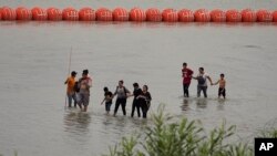 ARCHIVO - Migrantes que cruzaron el río Bravo desde México pasan junto a grandes boyas desplegadas como barrera fronteriza en el río en Eagle Pass, Texas, el 12 de julio de 2023. 