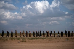 FILE - Men walk to be screened after being evacuated out of the last territory held by Islamic State militants, near Baghuz, Syria, Feb. 22, 2019.