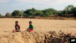 FILE —Children sit by a dug out water hole in a dry river bed in the remote village of Fenoaivo, Madagascar, November 11, 2020. The group World Weather Attributions blames climate change for a heatwave in October 2023.