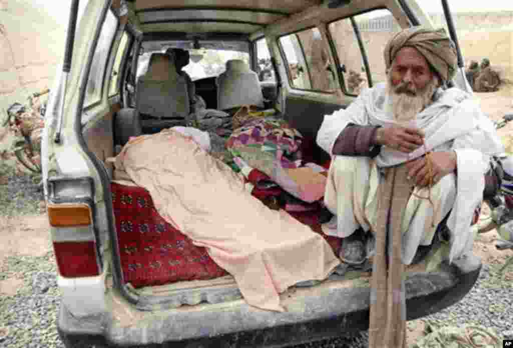 An elderly Afghan man sits next to the covered body of a person who was allegedly killed by a U.S. service member, in a minibus in Panjwai, Kandahar province south of Kabul, Afghanistan, Sunday, March 11, 2012. A U.S. service member walked out of a base i