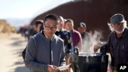 ARCHIVO - Un hombre de China recibe un plato de avena de un voluntario mientras espera con otros el procesamiento para solicitar asilo después de cruzar la frontera con México, el 24 de octubre de 2023, cerca de Jacumba, California.