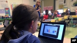 FILE - Fifth grader Ashlynn De Filippis, left, solves math problems on the DreamBox system as teacher Heather Dalton, center rear, works with other students in class at Charles Barnum Elementary School in Groton, Connecticut, Sept. 20, 2018.