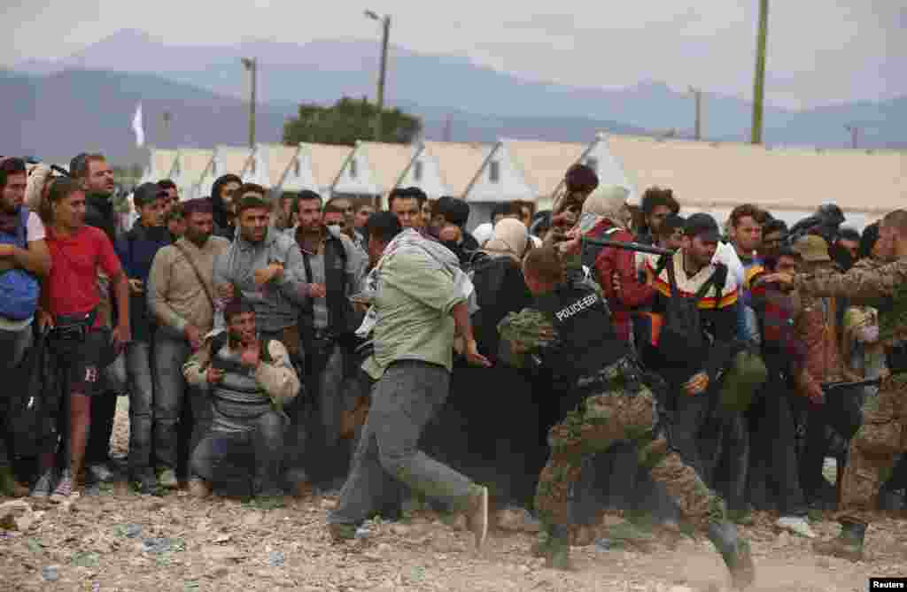 A policer officer hits a man with a baton as he tries to maintain order while migrants wait for trains at a temporary camp near Gevgelija, Macedonia, Sept. 7, 2015.