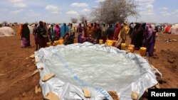 FILE - Internally displaced Somali women gather to collect water from a plastic pan after fleeing from drought-stricken regions, near a makeshift camp in Baidoa, west of Somalia's capital Mogadishu, March 26, 2017. 