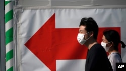 A man and a woman walks near a train station in Tokyo Thursday, April 30, 2020. Japan's Prime Minister Shinzo Abe expanded a state of emergency to all of Japan from just Tokyo and other urban areas as the virus continues to spread. (AP Photo/Eugene…