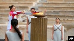 La campeona griega de esquí Paraskevi Ladopoulou (izquierda) enciende la antorcha durante la ceremonia de entrega de la llama olímpica, en el estadio Panathinean, en Atenas, Grecia, el 19 de octubre de 2021.