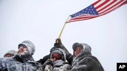 FILE - Military veterans huddle together to hold a United States flag against strong winds during a march to a closed bridge outside the Oceti Sakowin camp where people gathered to protest the Dakota Access oil pipeline in Cannon Ball, N.D., Dec. 5, 2016. 