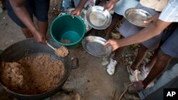 FILE - Students hold out their plates as the school cook ladles out a bulgur wheat and bean dish at a public school in Bombardopolis, Haiti. The WFP says 3.6 million Haitians face food insecurity.