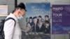Seorang perempuan berjalan melewati poster yang memperlihatkan anggota grup K-pop BTS di pusat informasi turis di Seoul pada 15 Juni 2022. China menangguhkan pemberian visa bagi warga Korea Selatan yang akan datang ke negara itu.(Foto: AFP/Jung Yeon-je)