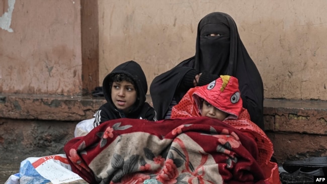FILE - A burqa-clad Afghan woman sits next to a boundary wall with her children as she seeks alms from people passing by along a road in Kabul, Jan. 8, 2022.