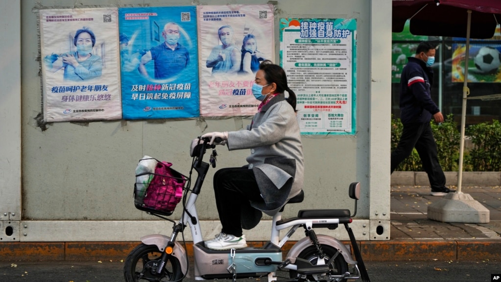 北京街头一名女子骑车路过墙上张贴的预防新冠病毒宣传画。（2022年10月26日）(photo:VOA)
