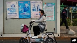 北京街头一名女子骑车路过墙上张贴的预防新冠病毒宣传画。（2022年10月26日）