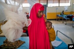 FILE - A woman holds a child at a clinic in Dollow, Somalia, Sept. 21, 2022.