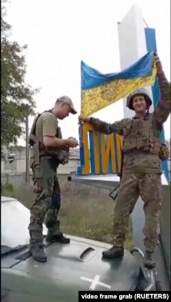 Ukrainian soldiers clamber onto a vehicle with the Ukrainian flag on the outskirts of the eastern town of Lyman, a long-time Russian bastion