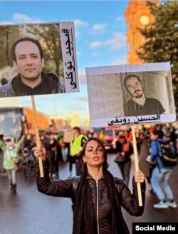 تصویر حسین رونقی و مجید توکلی در دست یکی از شرکت‌کنندگان تظاهرات جهانی حمایت از اعتراضات سراسری ایران