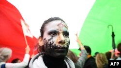 A protester wearing face-paint depicting France's iconic 'Marianne' leading an uprising, stands under a giant Iranian flag as people gather in support of Kurdish woman Mahsa Amini during a protest, Oct. 2, 2022 on Place de la Republique in Paris, followin