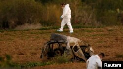 FILE - Forensic experts walk in a field after a bomb blew up a car and killed investigative journalist Daphne Caruana Galizia, in Bidnija, Malta, Oct. 16, 2017.