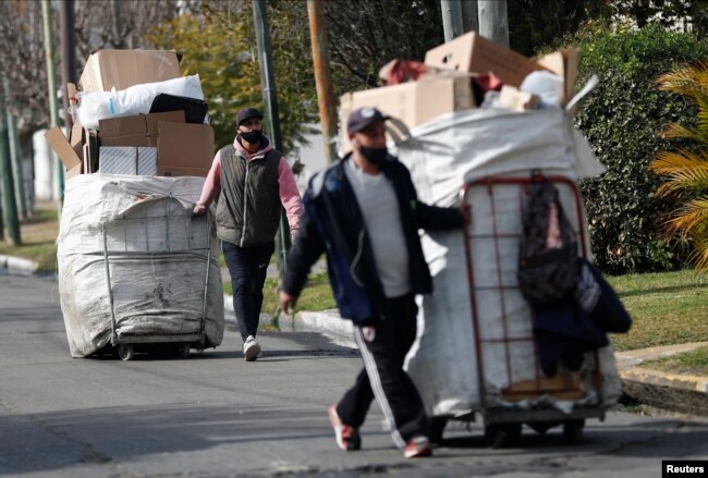 Garbage recyclers push their carts filled with plastic and cardboard as they arrive to the meeting point where they load their carts to a truck carrying it for recycling, in Lomas de Zamora, in the outskirts of Buenos Aires, Argentina July 8, 2022. (REUTERS/Agustin Marcarian)