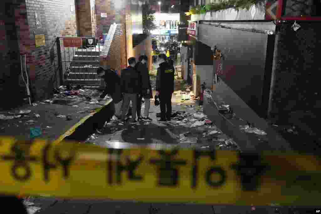 Police officers inspect the scene where people died and were injured in Seoul, South Korea, Oct. 30, 2022, after a mass of mostly young people celebrating Halloween festivities in Seoul became trapped and crushed as the crowd surged into a narrow alley. 