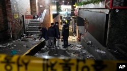 Police officers inspect the scene where people died and were injured in Seoul, South Korea, Oct. 30, 2022, after a mass of mostly young people celebrating Halloween festivities in Seoul became trapped and crushed as the crowd surged into a narrow alley. 