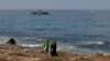 People walk along the beach as an Israeli navy vessel patrols the Mediterranean waters off Rosh Hanikra, known in Lebanon as Ras al-Naqura, on the Israeli side of the border between the two countries, on Oct. 7, 2022.