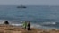 People walk along the beach as an Israeli navy vessel patrols the Mediterranean waters off Rosh Hanikra, known in Lebanon as Ras al-Naqura, on the Israeli side of the border between the two countries, on Oct. 7, 2022.