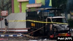 Seorang polisi memasang garis polisi di sebelah kendaraan yang dibakar di luar stadion Kanjuruhan di Malang, Jawa Timur pada 2 Oktober 2022. Sedikitnya 127 orang tewas ketika para pendukung yang marah menyerbu lapangan sepak bola setelah pertandingan anta