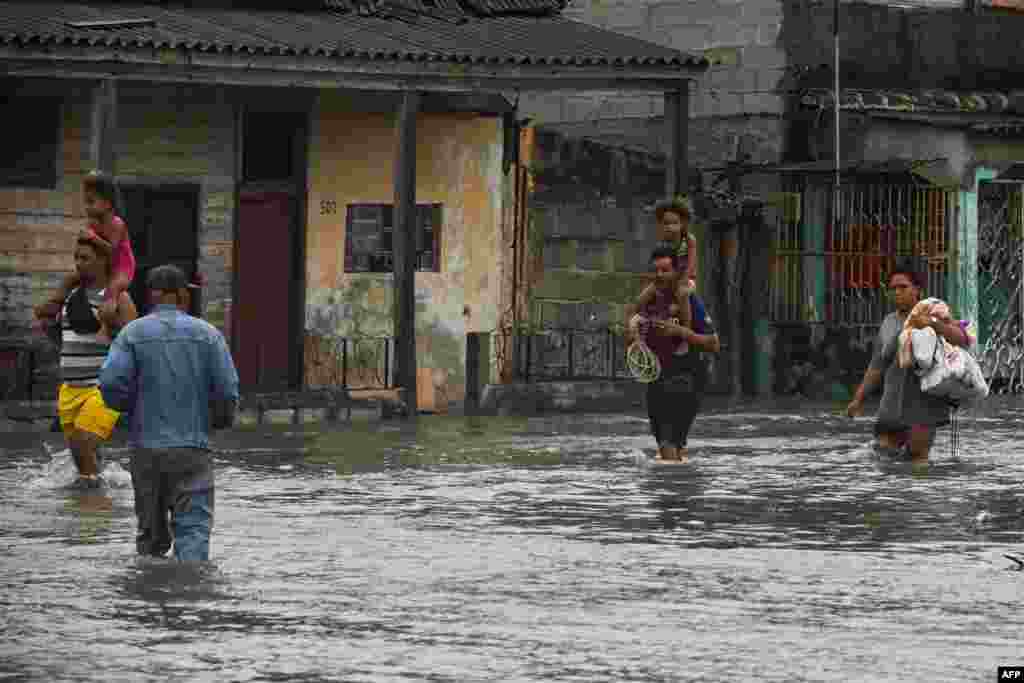 Varias personas caminan por una calle inundada en Batabanó, Cuba, el 27 de septiembre de 2022, durante el paso del huracán Ian. (Foto de YAMIL LAGE / AFP)