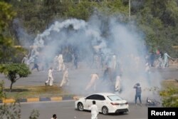 FILE - Supporters of the Pakistan Tehreek-e-Insaf (PTI) political party run with batons amid the tear gas smoke fired by police to prevent them from attending the protest march planned by ousted Prime Minister Imran Khan in Islamabad, in Rawalpindi, Pakistan, May 25, 2022.