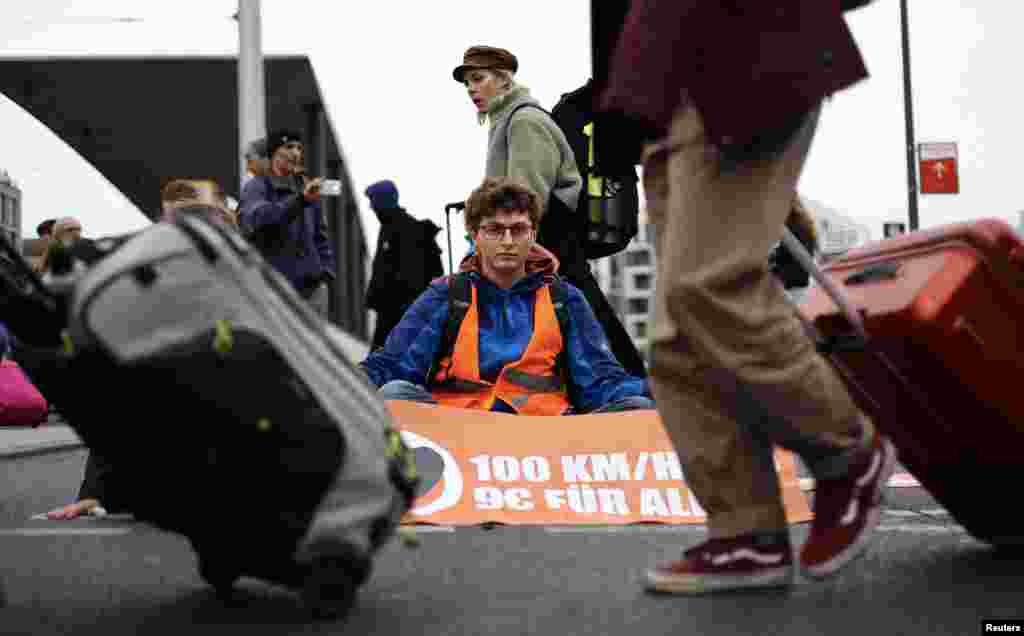 Passengers pull their trolleys past an environment activist of &quot;Last Generation&quot; who glued himself to a street outside the main railways station during climate change protests in Berlin, Germany.