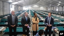 New York City Emergency Management Commissioner Zach Iscol, far right, and other officials talk with reporters in the sleeping area of the city's latest temporary shelter on Randall's Island, Oct. 18, 2022.