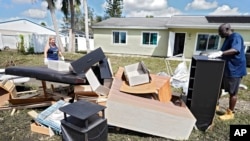 Andre McCourt, right, and his wife, Sandra, carry waterlogged furniture out of his house, Oct. 4, 2022, in North Port, Fla.