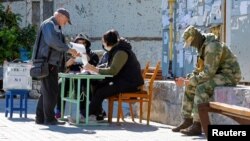 A local resident receives a ballot from members of an electoral commission before casting his vote into a mobile ballot box on the third day of a referendum on the joining of the self-proclaimed Donetsk People's Republic (DPR) to Russia, in Mariupol, Ukra