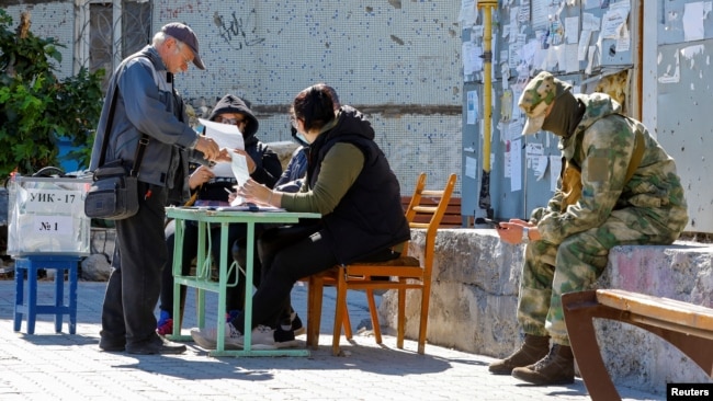 A local resident receives a ballot from members of an electoral commission before casting his vote into a mobile ballot box on the third day of a referendum on the joining of the self-proclaimed Donetsk People's Republic (DPR) to Russia, in Mariupol, Ukra