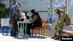 A local resident receives a ballot from polling workers before casting his vote into a mobile ballot box on the third day of a referendum on four Russia-occupied Ukrainian regions joining Russia, in Mariupol, Ukraine, Sept. 25, 2022.