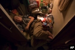 FILE - A man sleeps in his tiny "shoebox" apartment, where he cannot stretch out his legs, in Hong Kong, March 28, 2017.