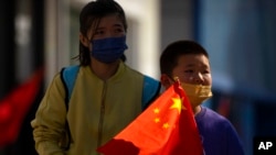 A boy wearing a face mask carries a Chinese flag as he walks along a pedestrian shopping street in Beijing, Oct. 6, 2022.