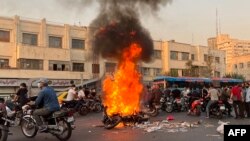 A picture obtained by AFP outside Iran, shows people gathering next to a burning motorcycle in the capital Tehran on October 8, 2022.