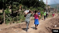 Por una polvorienta carretera rasgada, unas mujeres caminan cargando una pesada bolsa de alimentos donada.