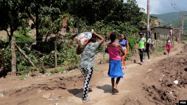 Por una polvorienta carretera rasgada, unas mujeres caminan cargando una pesada bolsa de alimentos donada.