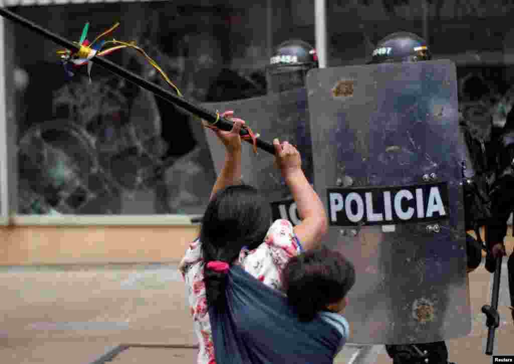 An Embera Indigenous woman carrying a child clashes with riot police while fighting for the right to land they say belongs to them, in Bogota, Colombia, Oct. 19, 2022. 