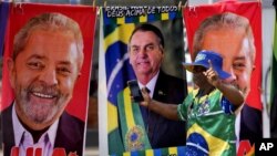 Un manifestante vestido con los colores de la bandera brasileña camina frente a unas toallas de un vendedor ambulante que muestran a los candidatos presidenciales brasileños, en Brasilia, el martes 27 de septiembre de 2022. (AP Foto/Eraldo Peres)