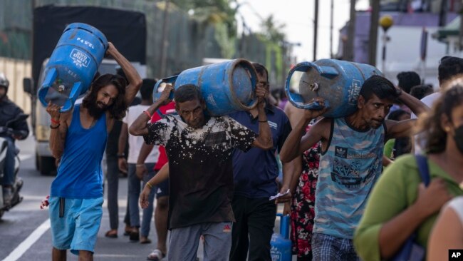 FILE - People carry gas cylinders after they bought it at a distribution center, in Colombo, Sri Lanka, July 12, 2022. Most Asian countries are prioritizing keeping the country running, no matter the energy source.