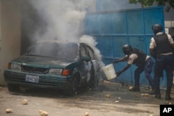 FILE - A police officer throws water on a burning vehicle in the parking lot of the police headquarters during a protest to demand the resignation of Prime Minister Ariel Henry in the Petion-Ville area of Port-au-Prince, Haiti, Oct. 3, 2022.