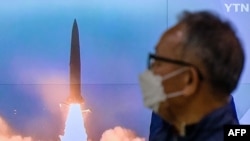 A man stands near a television screen showing a news broadcast with file footage of a North Korean missile test, at a railway station in Seoul on Oct. 9, 2022.