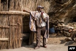 Ndlovu, 40 ans, habitant du site des grottes de Kome, pose avec un coq devant des habitations, dans le district de Berea, au Lesotho, le 9 octobre 2022.