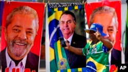 FILE - A demonstrator dressed in the colors of the Brazilian flag stands in front of towels for sale featuring Brazilian presidential candidates current President Jair Bolsonaro, center, and former President Luiz Inacio Lula da Silva, in Brasilia, Brazil, Sept. 27, 2022. 