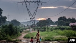 FILE - A woman and her son walk in front of a transmission tower in a remote area near Mbanza-Ngungu, Democratic Republic of Congo, Dec. 25, 2018.